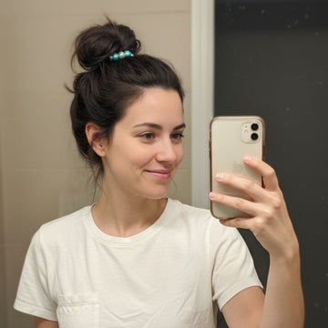 Woman taking a mirror selfie with a phone, wearing a white t-shirt.