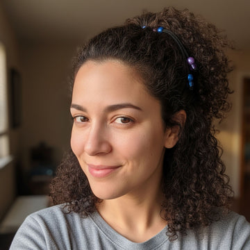 Woman with curly hair wearing a headband, smiling indoors.