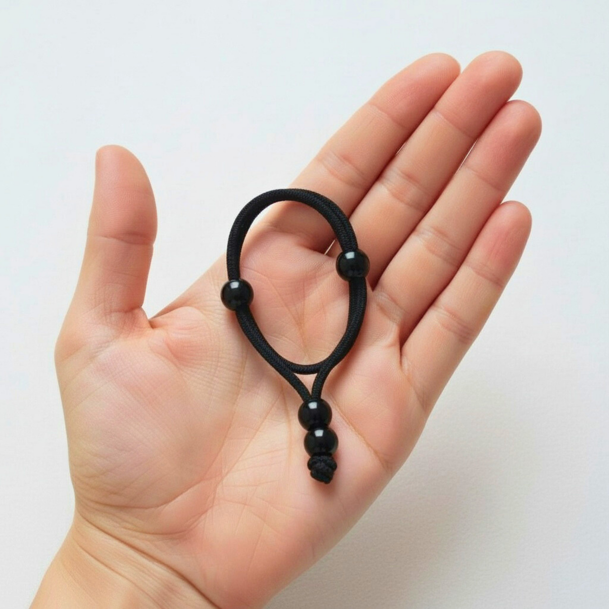 Black hair tie with decorative elements held in a hand against a white background