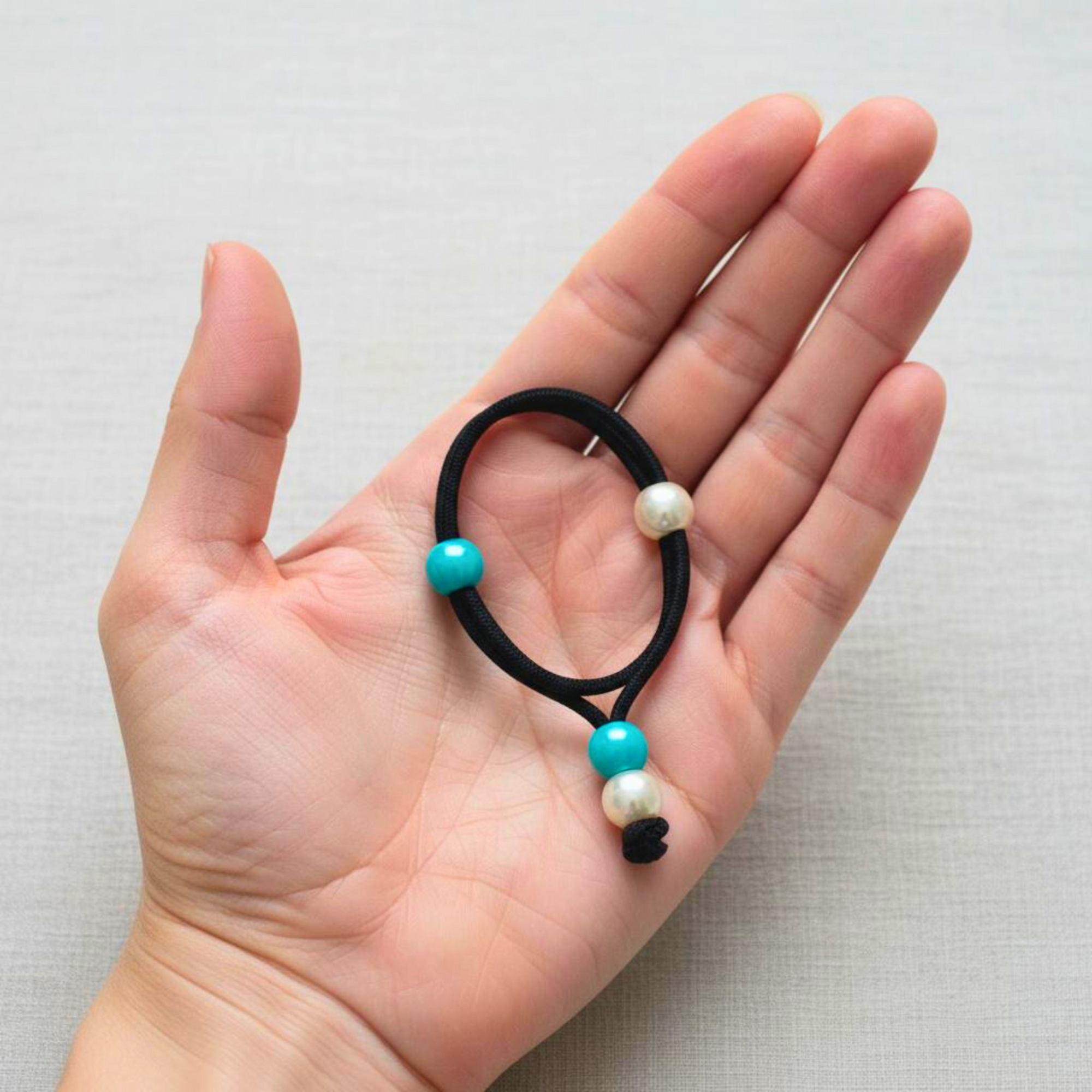 Hair tie with white and teal beads held in a hand on a light background