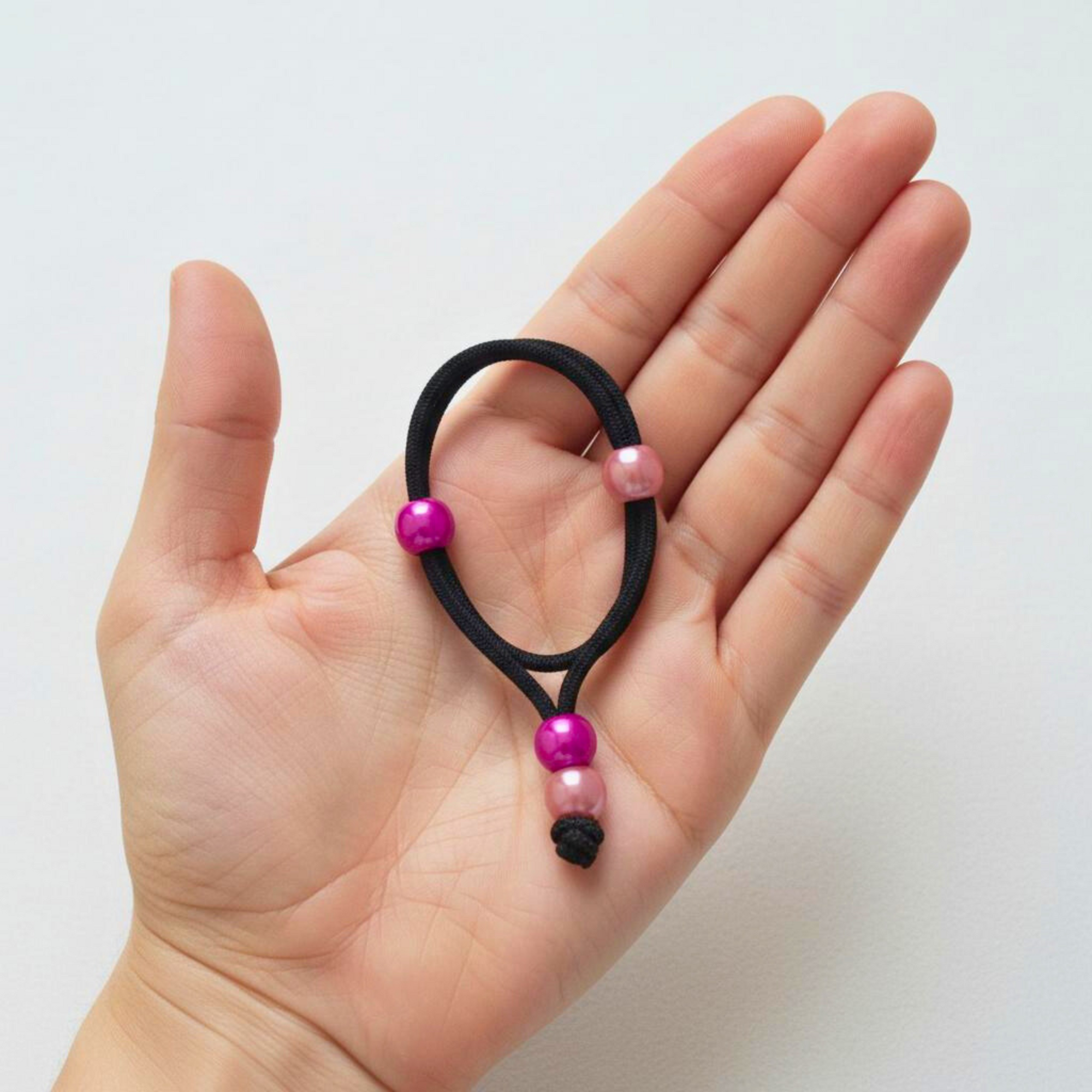 Hand holding a black hair tie with light pink beads and vibrant pink beads against a white background