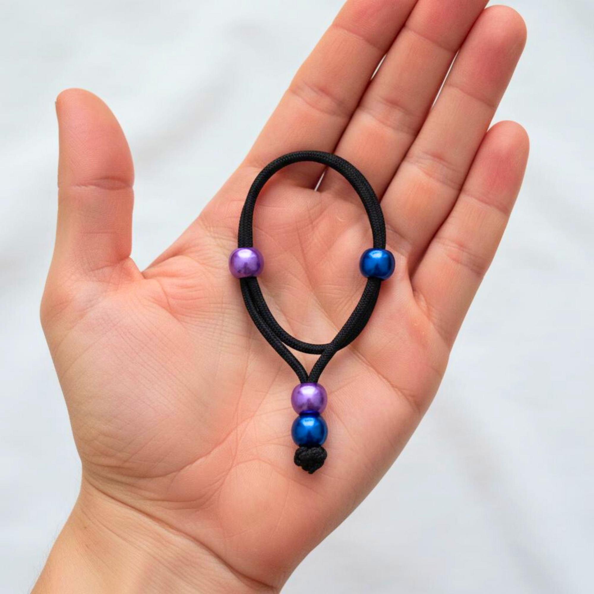 Black hair tie with purple and blue beads held in a hand against a white background