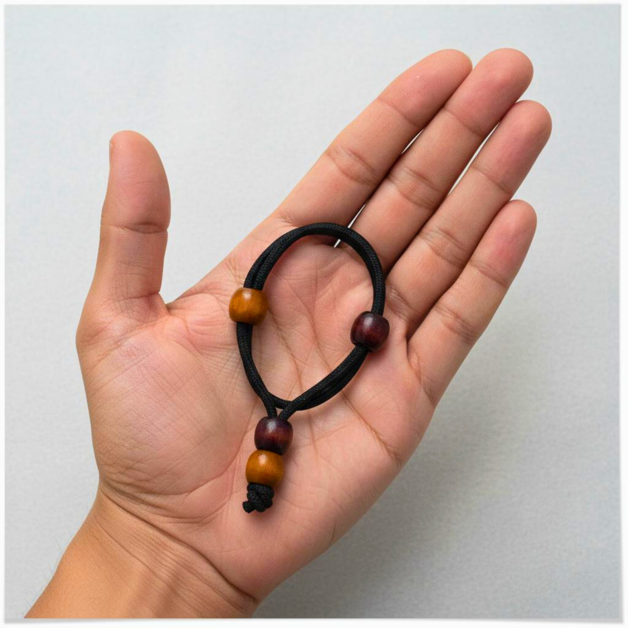 Hand holding a black hair tie with wooden beads against a light gray background