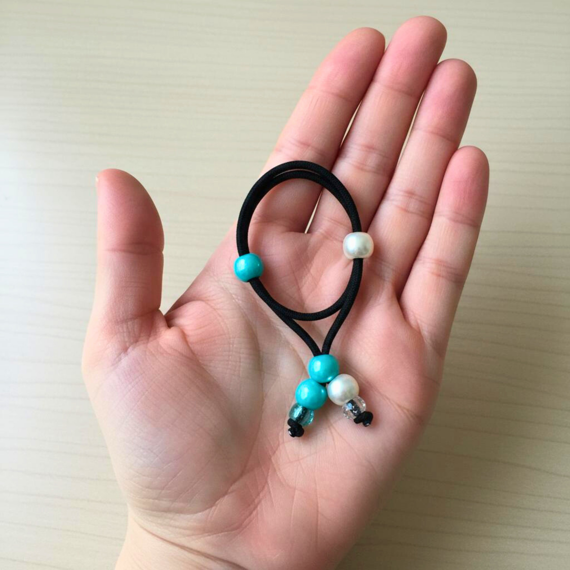 Hair tie with white and teal beads held in a hand on a light background