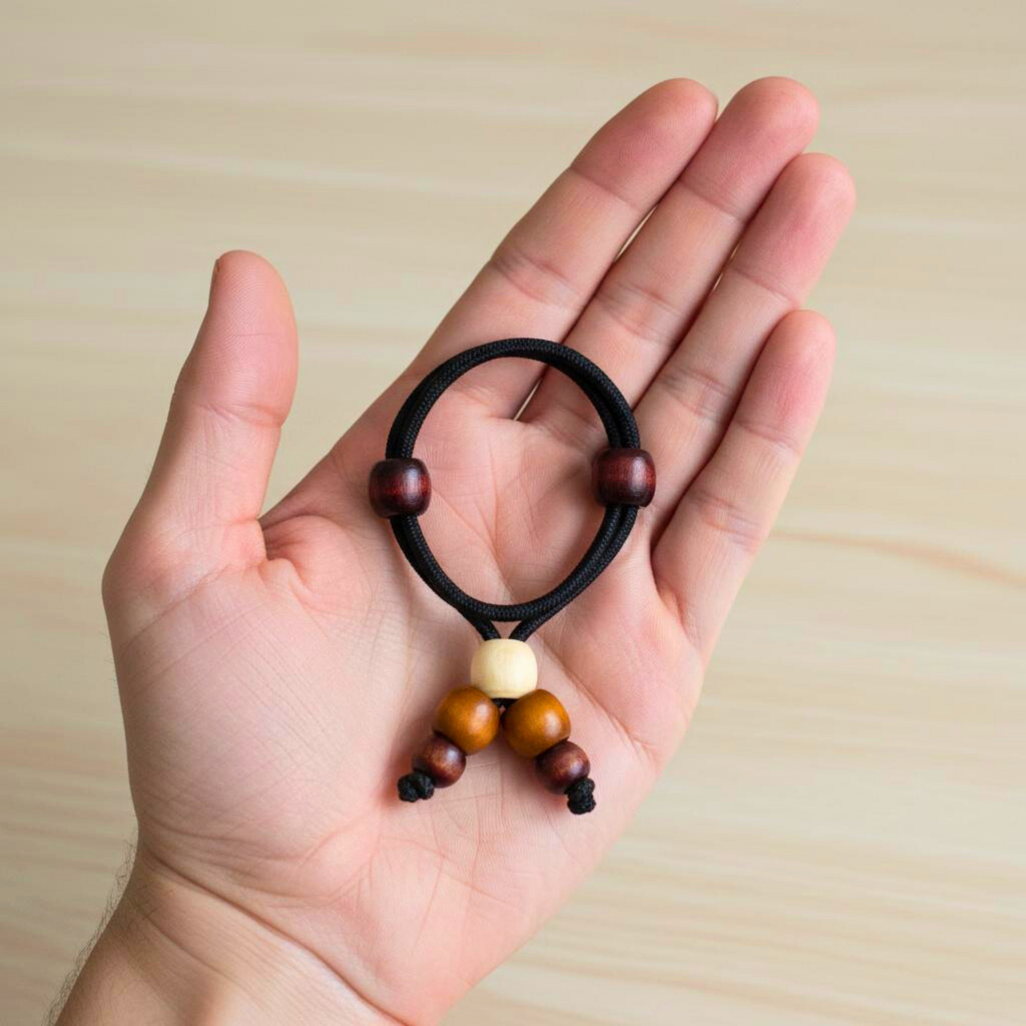Hand holding a black hair tie with wooden beads against a light wood background