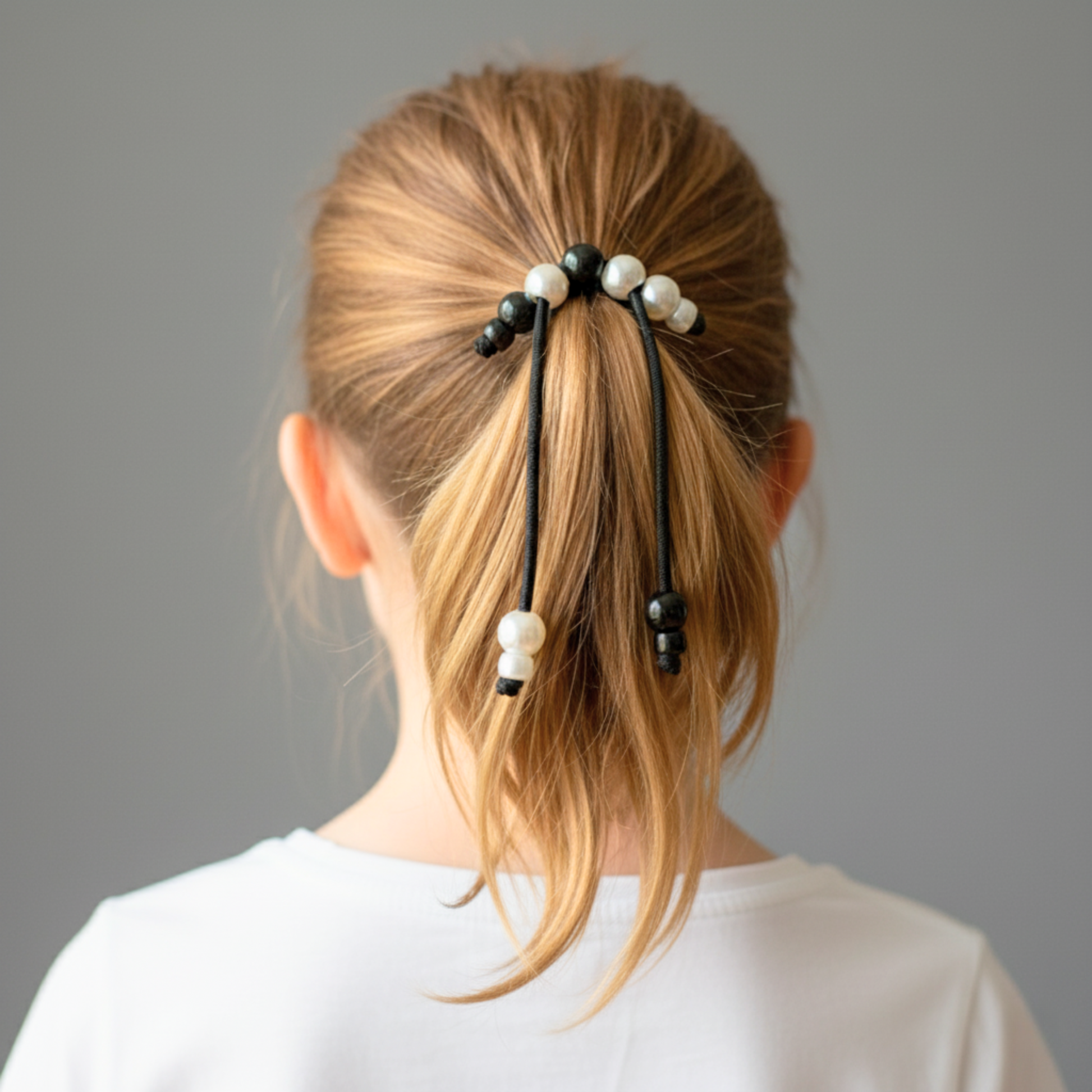 Person with a ponytail using hair ties with pearls against a gray background