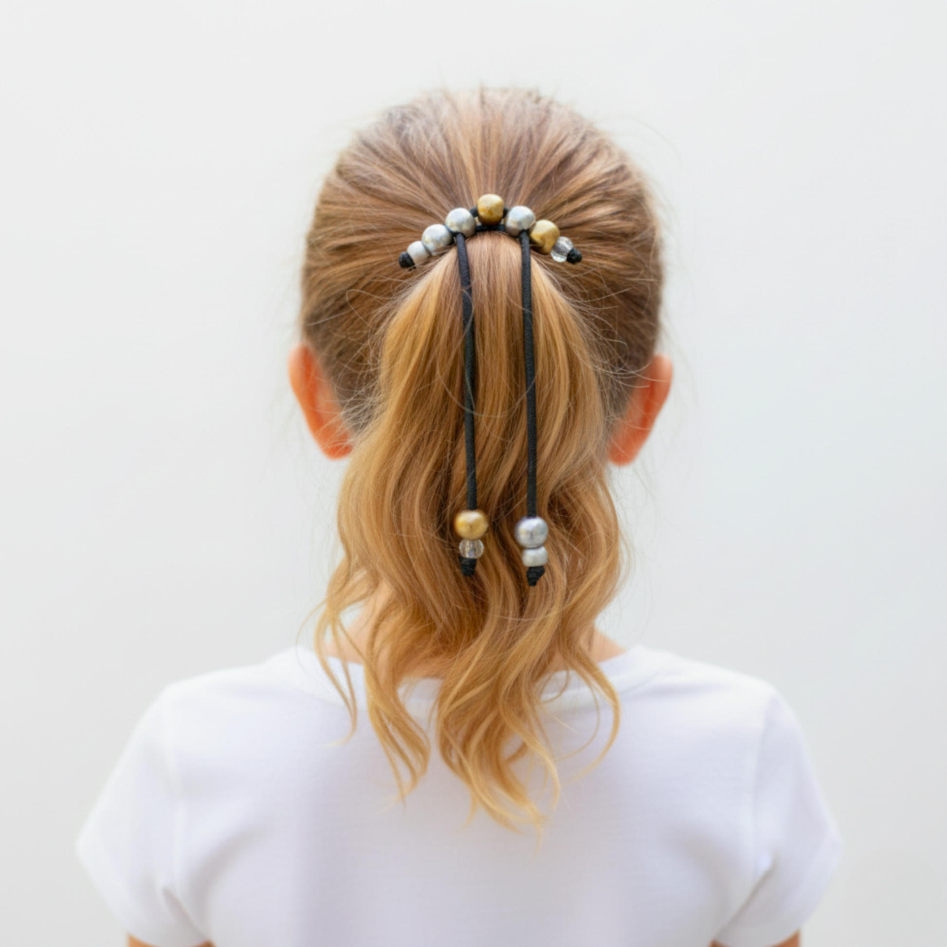 Child with blonde hair styled in a ponytail with decorative beads against a white background