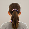 Person with a ponytail using colorful hair ties on a plain background