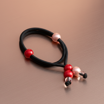 Black hair tie with red and pink beads on a brown background