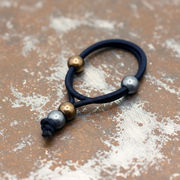 Navy blue hair tie with gold and silver beads on a gray background