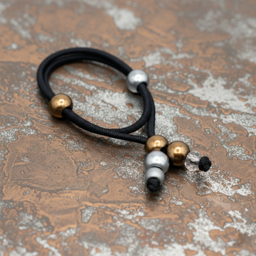 Black hair tie with gold and silver beads on a gray background
