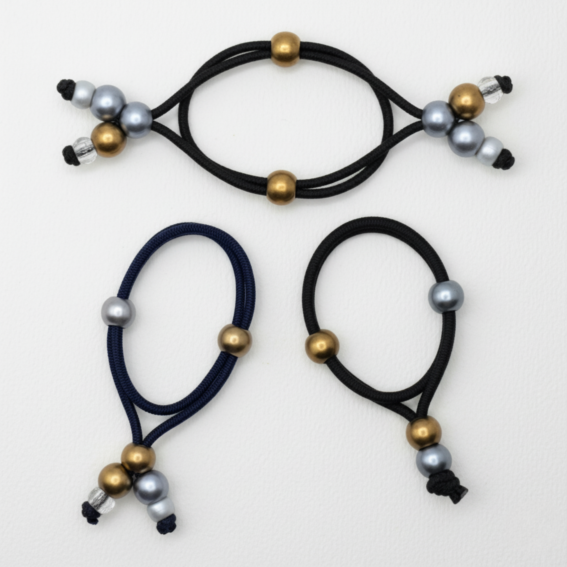 Three navy blue hair ties with gold and silver beads on a white background