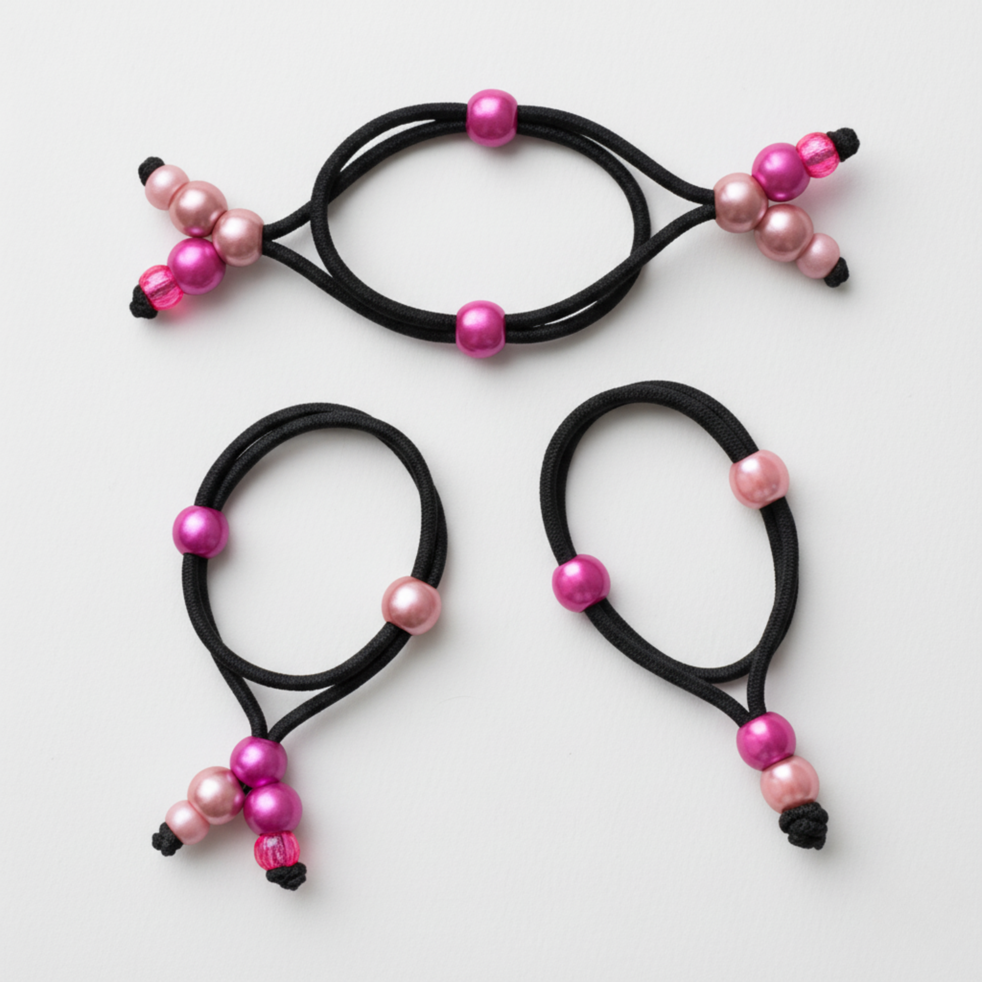 Three black hair ties with pink and black beads on a white background