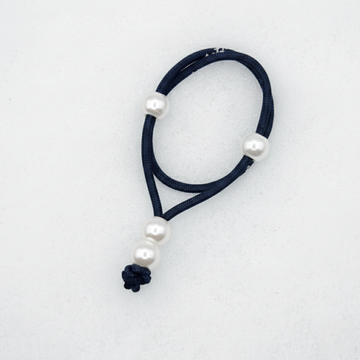 Navy blue hair tie with white pearls on a light blue background