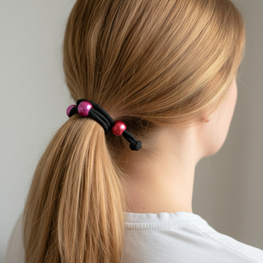 Person with a ponytail held by a hair tie with pink beads against a neutral background