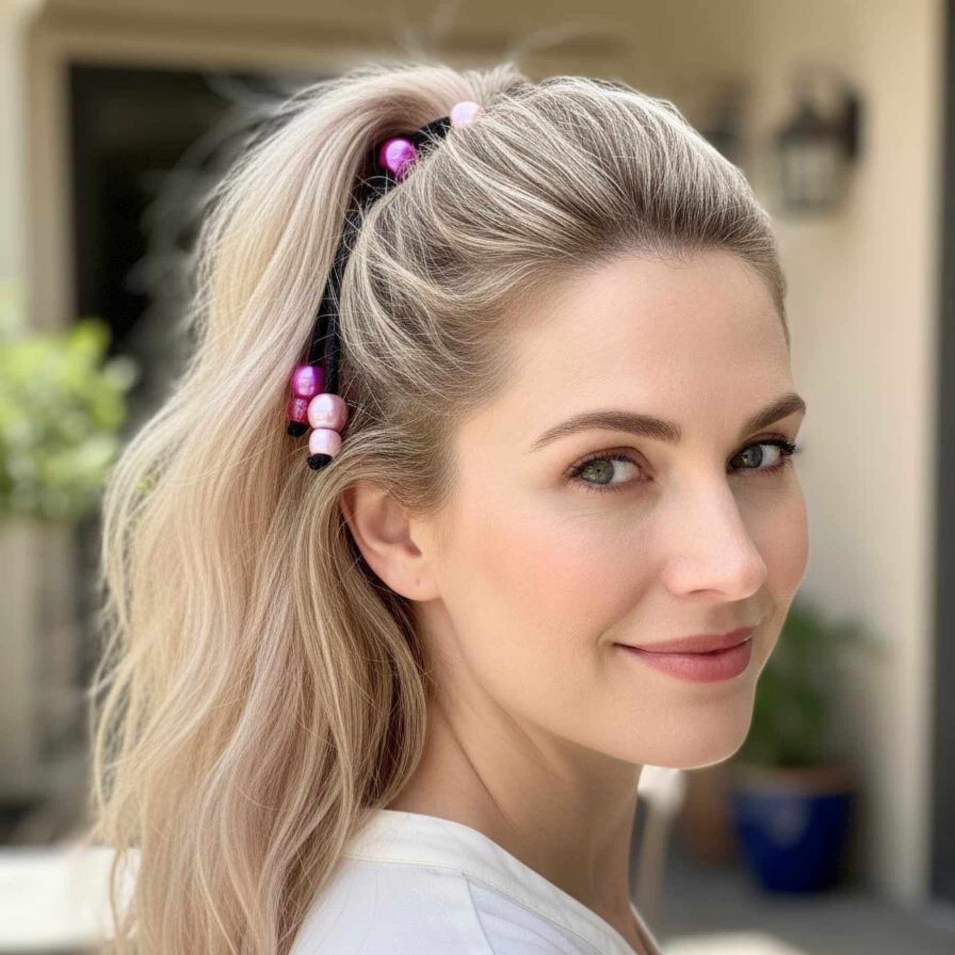 Woman with blonde hair in a ponytail with colorful hair ties, smiling outdoors.