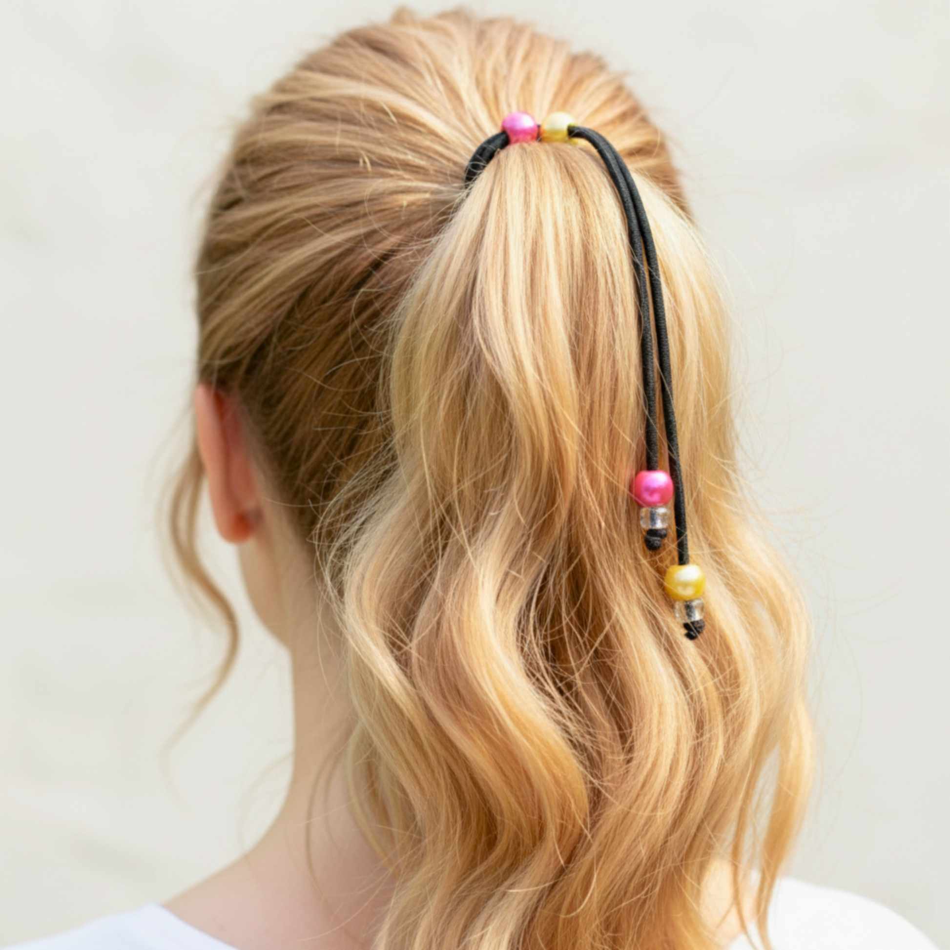 Person with blonde hair tied back using a colorful hair tie against a plain background