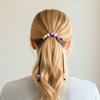 Person with a ponytail using decorative hair ties against a plain background