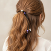 Person with wavy brown hair tied in a ponytail with decorative hair ties against a neutral background