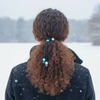Person with curly hair tied back with colorful hair ties in a snowy landscape