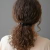 Person with wavy hair tied back in a ponytail against a neutral background