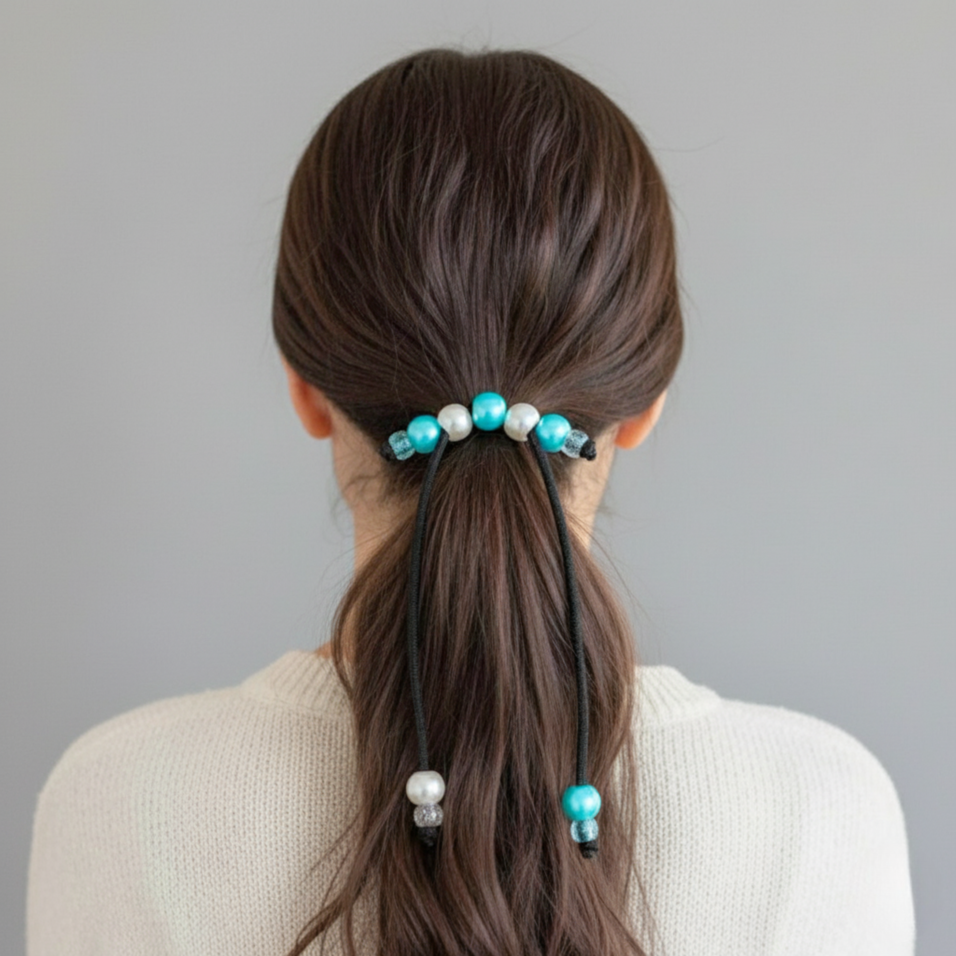 Person with a ponytail held with a decorative hair tie against a gray background