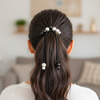 Person with hair styled in a ponytail using decorative hair ties in a blurred indoor setting