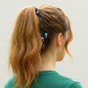 Person with a ponytail wearing colorful hair ties against a plain background