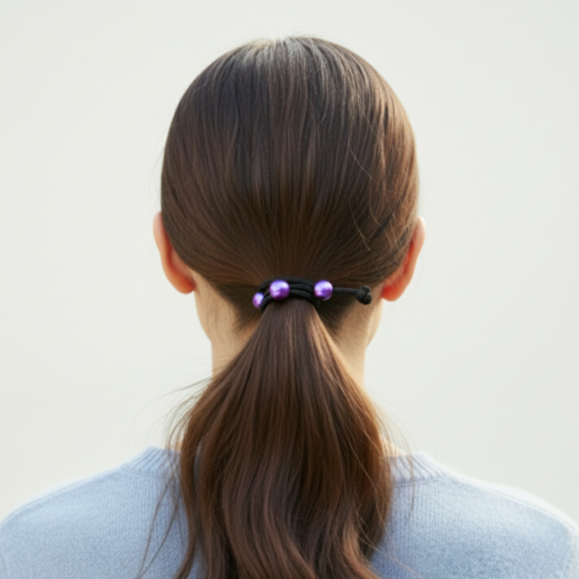 Person with a ponytail held by a hair tie against a plain background