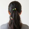 Person with a ponytail using colorful hair ties on a plain background