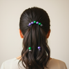 Person with a ponytail adorned with colorful hair accessories against a neutral background